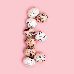 Letters E from Easter Quail eggs pink colored. Spring Easter composition with chocolate food. Monochrome image