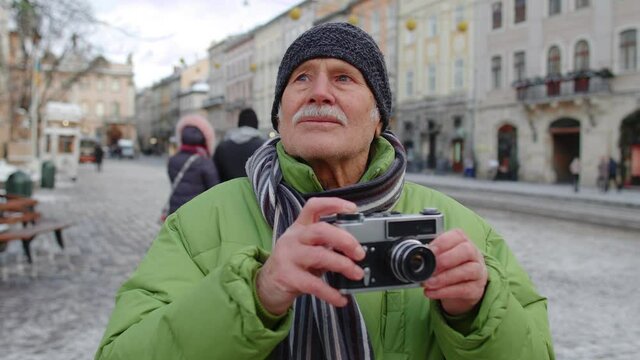 Senior man grandfather taking pictures with photo camera, smiling using retro device outdoors in winter city center of Lviv, Ukraine. Photography, travelling, vacation, trip, Christmas holidays eve