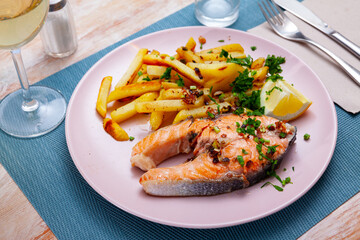 Italian dish of tasty steak of baked salmon with french fries on plate