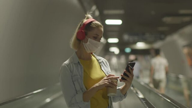 Woman going on a plane with her suitcase. Listening to music with ears. She wears a medical mask to protect it from the virus.