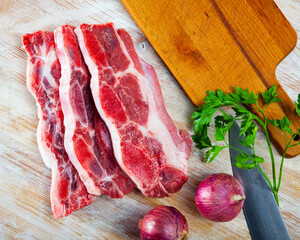 Raw beef with streaks of fat on kitchen table with red onion, garlic and parsley