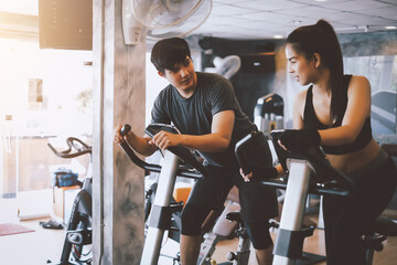 Asian man and woman they are enjoys cycling in the gym because it keeps his legs strong and healthy.