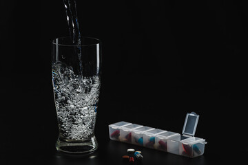 a glass of water and pills. A daily intake of. On a black background