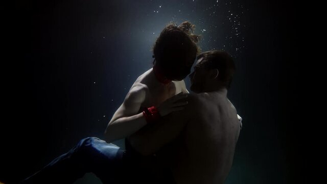 Sensual couple swim and spin underwater. A man passionately hugs and kisses a woman. There are a lot of bubbles floating around.