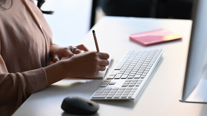 Close up view of businesswoman working in office with computer and writing business plan in notebook.