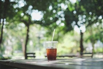 a plastic cup of iced americano (black coffee) on the wood plank table in the garden