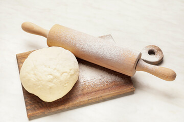 Fresh dough and rolling pin on light background