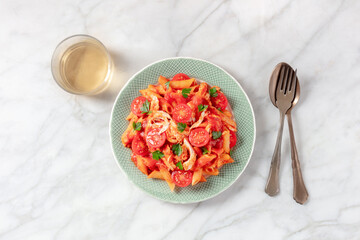 Penne pasta with chicken, tomato sauce and parsley, shot from above with a glass of wine