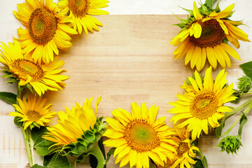 Frame made of beautiful sunflowers on light wooden background
