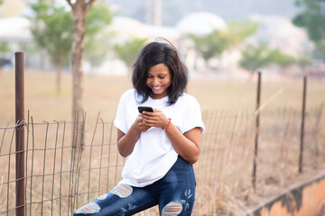 Fototapeta premium beautiful young african lady smiling while reading content on her phone