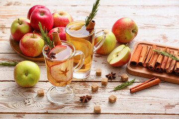 Tasty drink with spices and apple slices in cups on wooden background