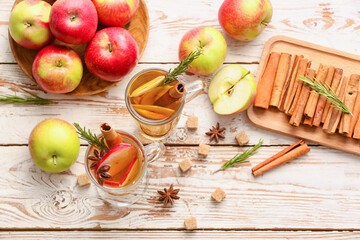 Tasty drink with spices and apple slices in cups on wooden background
