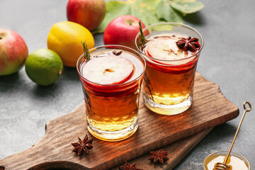 Tasty drink with spices and apple slices in glasses on dark background