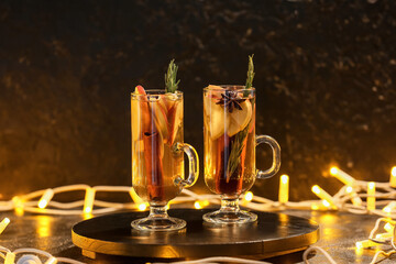 Tasty drink with spices and apple slices in cups on table at night