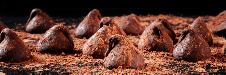 Chocolate truffles panorama, side view on a dark background