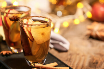 Tasty drink with spices and apple slices in glasses on wooden table at night