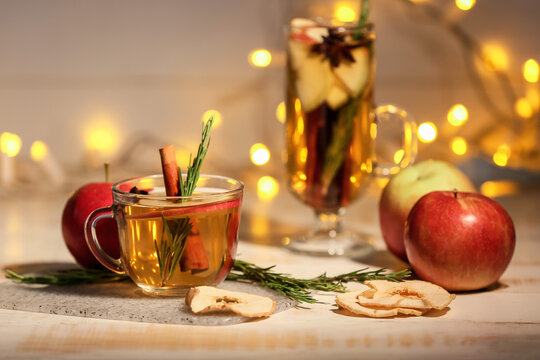 Tasty drink with spices and apple slices in cup on wooden table at night