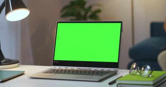 open laptop with green screen on working table in living room, man is turning off lamp at background, zoom shot