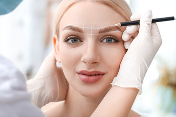 Young woman undergoing eyebrow correction procedure in beauty salon
