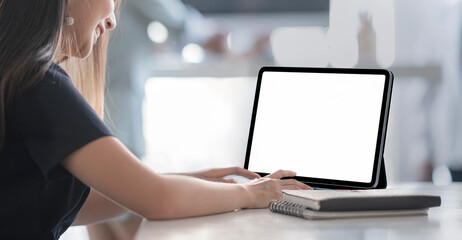 Cropped shot of young woman working on tablet computer while stay at home. Blank screen for graphic design.