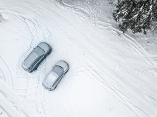 Frozen car and SUV at winter season. Aerial top down view of the two snow-covered vehicles parked on snow surface after blizzard. White landscape, cold weather.
