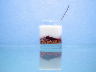 Healthy food for breakfast. Yogurt with muesli in a glass with a spoon on a glassy surface with reflection.