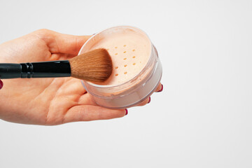 Female palm holding loose face powder jar against gray background