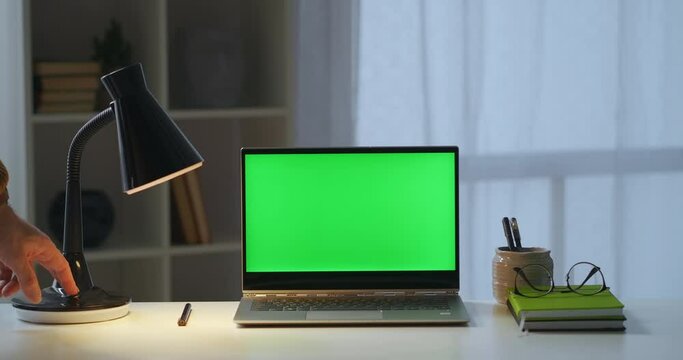 man is closing cover of laptop with green screen on table, freelance and home office, working place of writer or freelancer in apartment