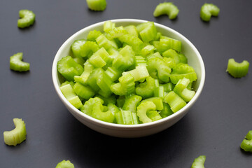 Slices of celery in bowl on dark background.