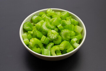 Green fresh celery pieces in white bowl on dark background.