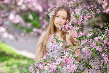 Obraz premium Cute little pensive girl with handmade hair wreath on her head smelling flowers in the spring blossom garden, close-up