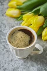 cup of black coffee on stone surface and bouquet of yellow tulips