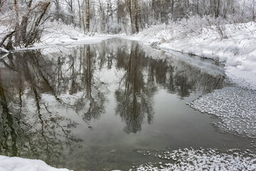 Winter landscape with river and forest reflected in the freezing water. Cloudy winter day. a dim photo taken in the Middle Urals, Russia. Silence, contemplation and harmony in a snowy nature