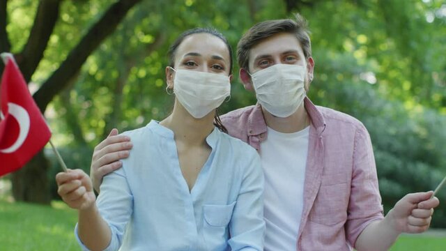 Two young people are waving the Turkish flag while looking at the camera. They wear a medical mask to protect them from the virus.