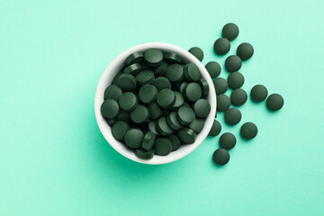 Bowl with spirulina pills on mint background, top view