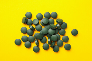 Heap of spirulina pills on yellow background, top view