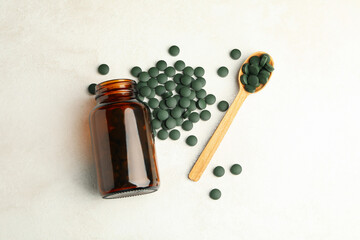 Bottle and wooden spoon with spirulina pills on white textured background