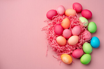 Painted Easter eggs in decorative nest on pink background