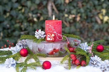Weihnachtsdekoration mit Eislaterne, roter Kerze und Hagebutten