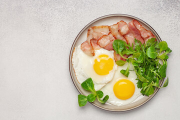Continental breakfast - fried eggs, bacon and lettuce leaves in a plate on a bright background. Top View