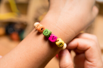 Words concept, String a bracelet Wooden letter beads of LOVE word. Close up woman hand string color Wooden letter beads.
