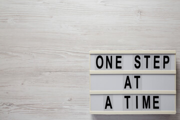 'One step at a time' on a lightbox on a white wooden background, top view. Flat lay, overhead, from...