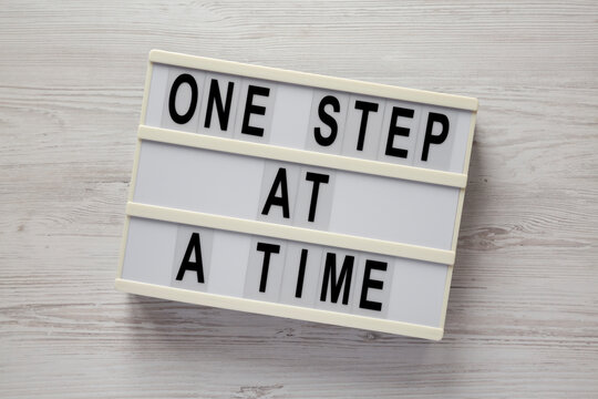'One step at a time' on a lightbox on a white wooden background, top view. Flat lay, overhead, from above.