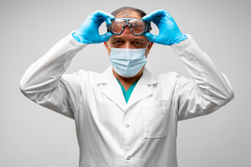 Male senior doctor in mask taking off protective glasses