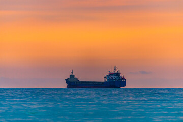 Cargo ship sailing away at the colorful sunset