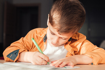 Cute 7 years old child doing his homework sitting by desk. Boy writing in notebook.