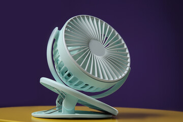 Modern electric fan on yellow table against violet background