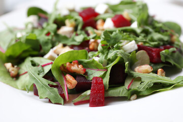 Delicious beet salad with arugula and walnuts on plate, closeup view
