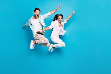 Photo of childish carefree young lovers dressed casual shirts jumping high arms hands sides...