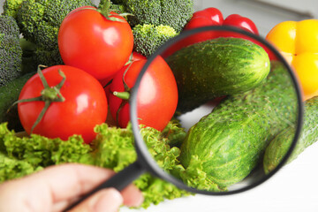 Woman with magnifying glass exploring vegetables, closeup. Poison detection